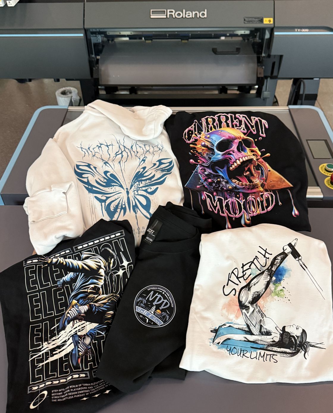 DTF-printed T-shirts and hoodies in front of the Roland TY-300 printer